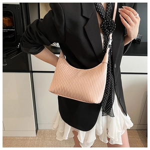 Close-up of pleated texture on light pink crescent bag held by a stylish model