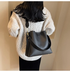 Detail of black matte leather bucket bag with wide shoulder strap and gold hardware