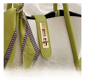 Detail of gold hardware lock on beige and green leather handbag with decorative silk scarf