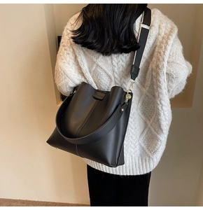 Detail of black leather bucket bag with wide knit shoulder strap worn by a model