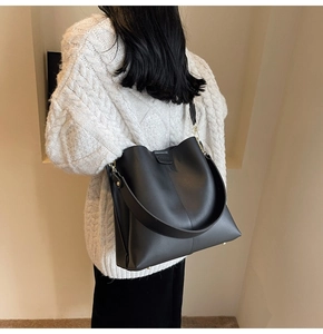 Detail view of large black leather bucket bag with gold hardware and protective metal feet
