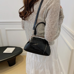 Detailed view of black vintage kiss-lock bag with embossed texture worn by a model