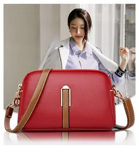 Detail of red lychee grain leather crossbody bag with brown strap and white stitching