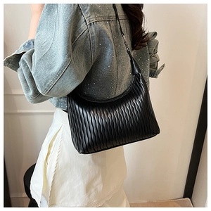 Side view of black pleated shoulder bag with wavy texture on female model in white interior