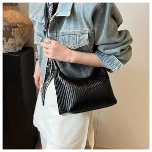 Detail of black pleated shoulder bag with sleek leather texture and wavy craftsmanship