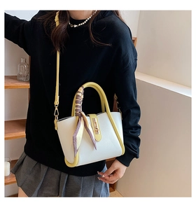 Close-up of white lychee leather bag with yellow handles and elegant purple silk scarf detail