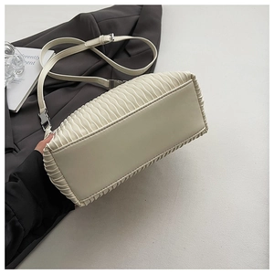 Detail view of cream pleated handbag with adjustable strap and flat rectangular base