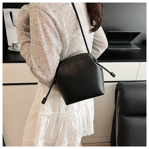 Close-up of black lychee grain crossbody dumpling bag worn by model in a minimalist setting