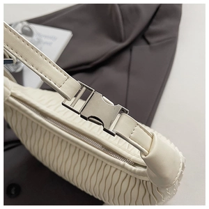 Detail of cream pleated underarm bag showing silver metal buckle and soft fabric texture