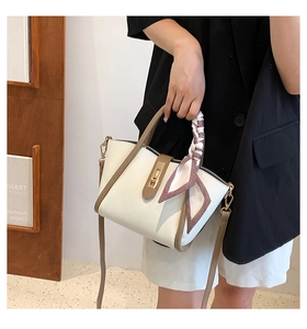 Detail of white lychee texture bag with brown trim, gold lock and silk ribbon handle