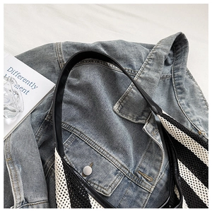 Close-up of black and white striped knit tote bag with leather strap on denim jacket