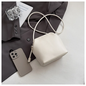Minimalist cream white lychee leather crossbody bag on a grey blazer with accessories