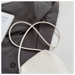 Detailed close-up of white lychee pattern leather shoulder bag on a gray blazer