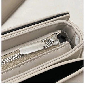 Close-up of a silver metal zipper and neat stitching on a beige crossbody bag