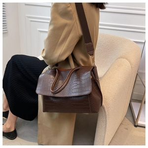 Détail du sac marron foncé à texture crocodile avec large bandoulière tissée chic