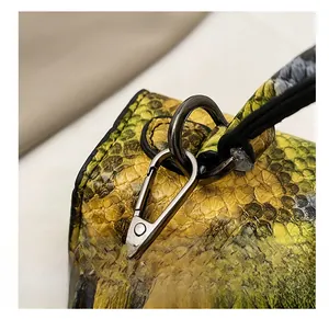 Macro shot of dark chrome spring hook hardware on green snake pattern leather bag