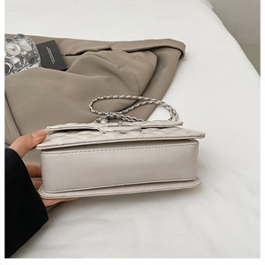 Detail of beige quilted shoulder bag with silver chain strap and metal swivel lock