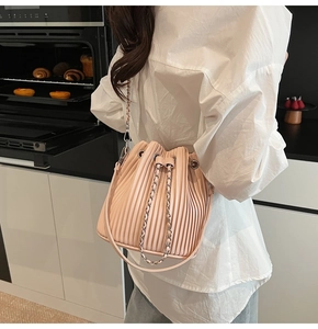 Detail of light pink pleated bucket bag with silver chain strap worn by a model