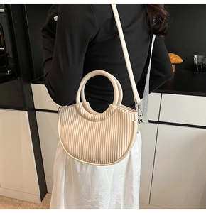 Close-up of beige pleated crescent handbag showing fine vertical textures and round handle