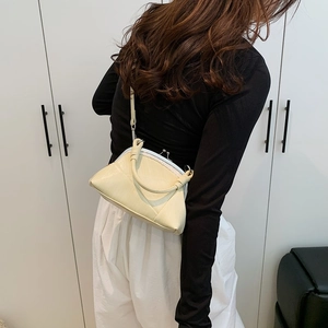 Detail showing the cream kiss-lock handbag with wrapped top handle and slim shoulder strap