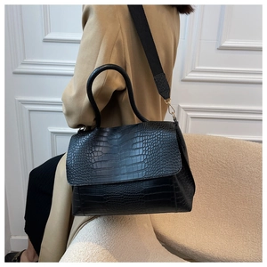 Detail of black crocodile pattern faux leather tote bag with wide strap and gold hardware
