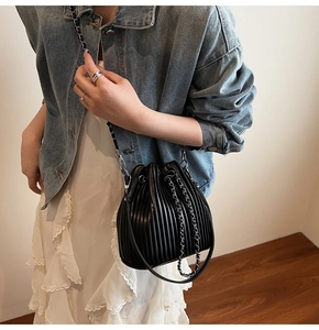 Detail of black pleated drawstring bucket bag with silver chain strap on model outfit