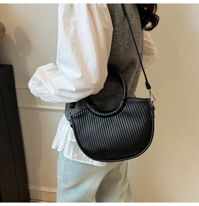 Detail of black pleated crescent handbag featuring a circular handle and slim strap