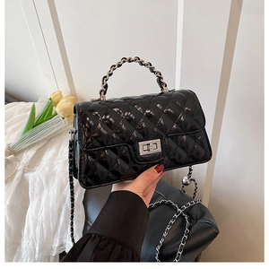 Close-up of black glossy quilted leather handbag with silver rotary metal lock and chain