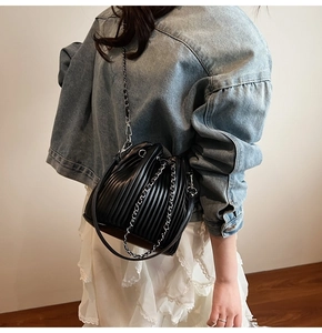 Detail of black pleated bucket bag with silver chain strap worn over a white lace skirt