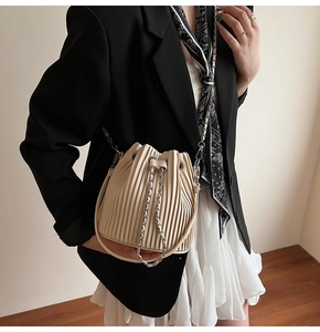 Detail of pleated beige bucket bag with silver chain strap and drawstring closure