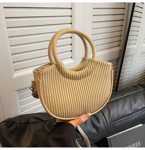 Close-up of beige pleated crescent bag with dual handles and smooth PU leather texture