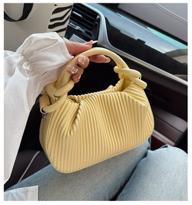Detail of light yellow pleated handbag with a knotted handle shown in a car interior