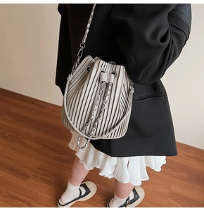 Detail of light grey pleated drawstring bucket bag with silver chain strap worn by model