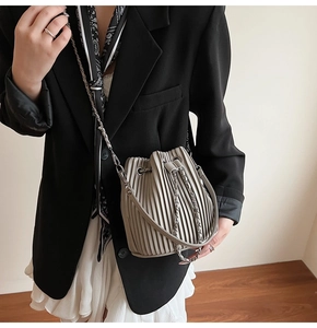 Detail view of the vertical pleats and sleek chain strap on the beige bucket bag