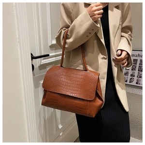 Détails d'un sac à bandoulière marron motif crocodile porté par un mannequin