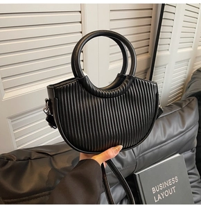 Detail of black pleated crescent handbag featuring metallic ring handles and leather texture