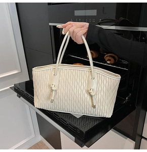 Detail einer cremefarbenen Ledertasche mit Wellenfalten und geknotetem Griff-Design