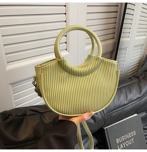 Detail of pistachio green pleated half-moon bag with elegant round handle and texture