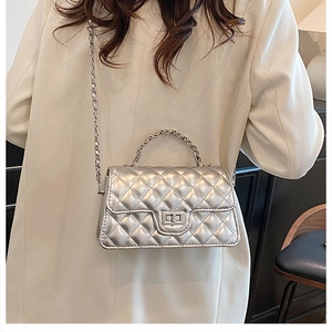 Detail of silver quilted crossbody bag with metal handle and woven chain strap on model