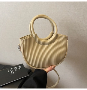 Detail of cream pleated crescent bag featuring round handle and silver D-ring hardware