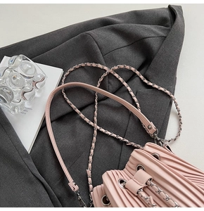 Detailed macro view of pink pleated bucket bag with metallic chain strap and eyelets