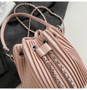 Close-up of pale pink pleated bucket bag showing vertical accordion texture and silver chain