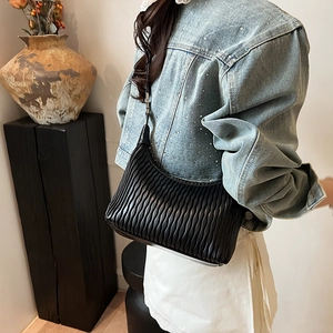 Chic black matelassé shoulder bag with textured pleats worn by a model in casual style