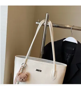 Close-up of white woven tote bag featuring a silver logo plate and a brown bear charm