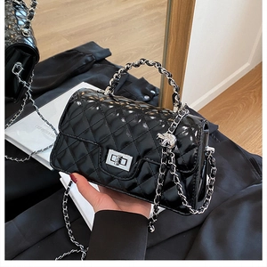 Close-up of black quilted glossy handbag with silver chain strap and twist lock detail