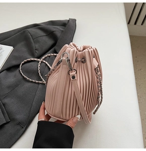 Close-up of pink pleated drawstring bucket bag with silver metal eyelets and chain strap
