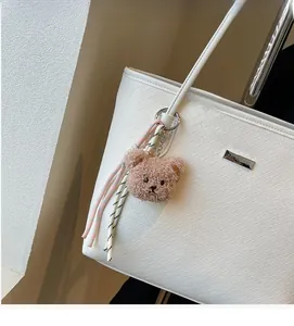 Close-up of white woven tote bag with a plush bear charm and striped ribbon detail
