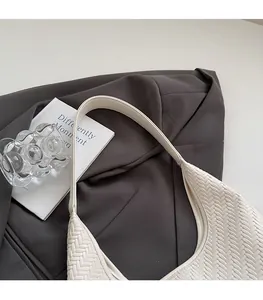 Close-up of white woven tote bag strap and leather texture on a grey blazer background