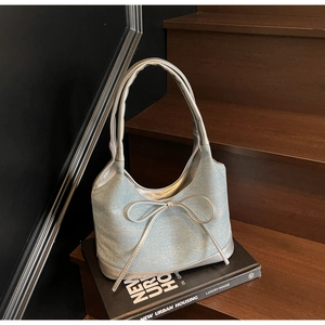 Detail of light blue denim tote bag with rhinestones, bow accent, and silver handles