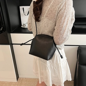 Minimalist black lychee pattern leather crossbody bag with drawstring closure shown on model